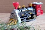 model toy train is posed against a plain brown background. Fresh greenery peeks into the foreground.