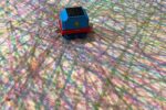 Detail of a painting made with a child's train toy with many layered colour lines made by train wheels